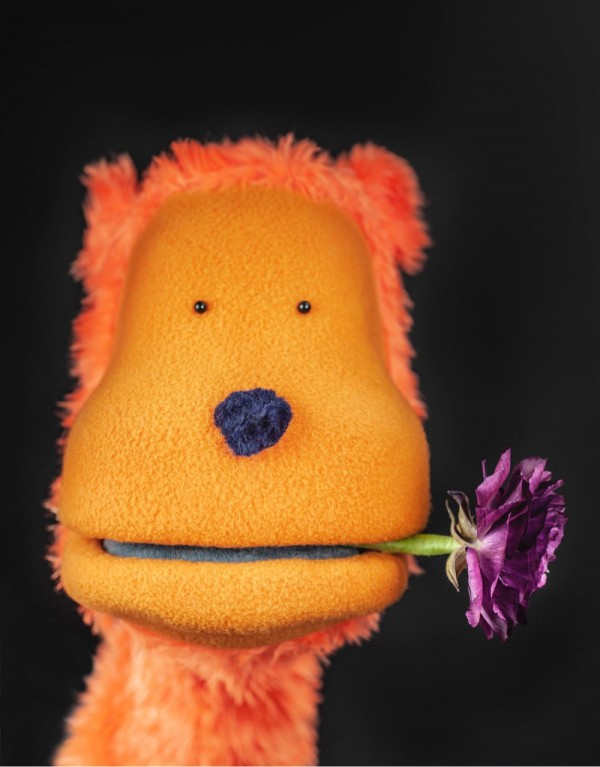 Den oransje hånd-dukken <q>Kriserådgiver</q> med en blomst i munnen