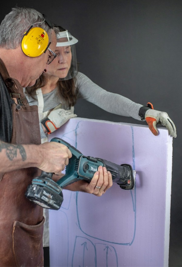 Tiina holds a foam plate while Sean uses an electric saw