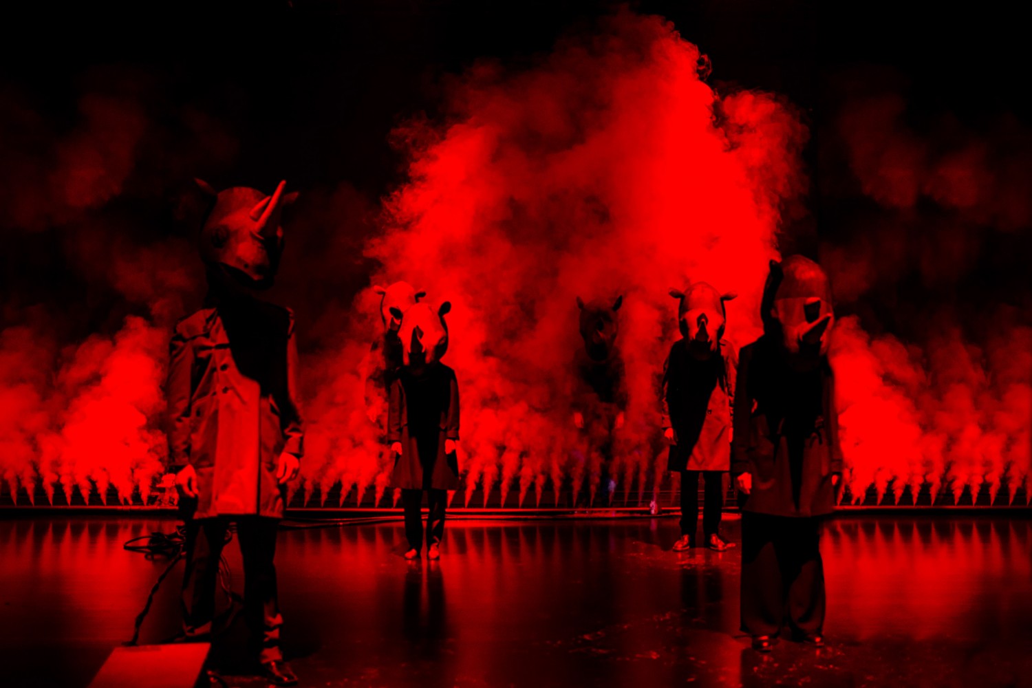 Skuespillere med neshornmasker står på en scene fylt med rødt lys og røyk